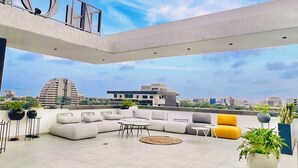 Amplia terraza en la azotea con mobiliario moderno, una planta grande en maceta y una vista despejada del horizonte urbano.