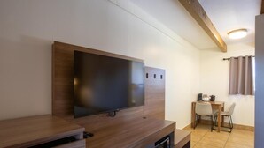Una habitación moderna con una televisión de pantalla plana montada en un mueble de madera, una pequeña mesa con sillas y un microondas debajo de la televisión.