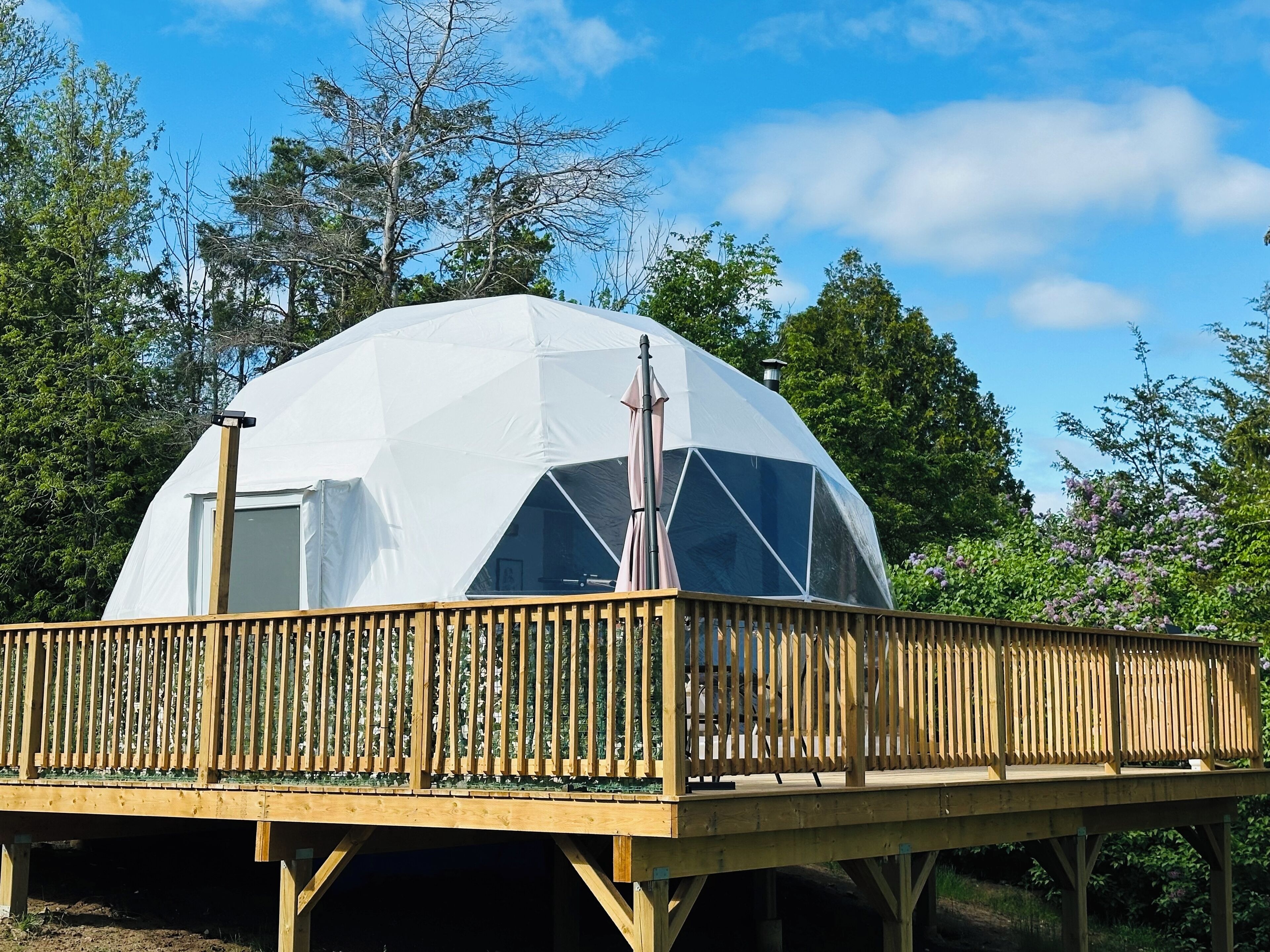 Une structure en forme de dôme géodésique, dotée d’une terrasse en bois et d’une rambarde en métal.