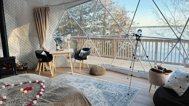 Een knus vertrek met een groot raam, een houten terras, een telescoop en een kaarsdecoratie in de vorm van een hart.