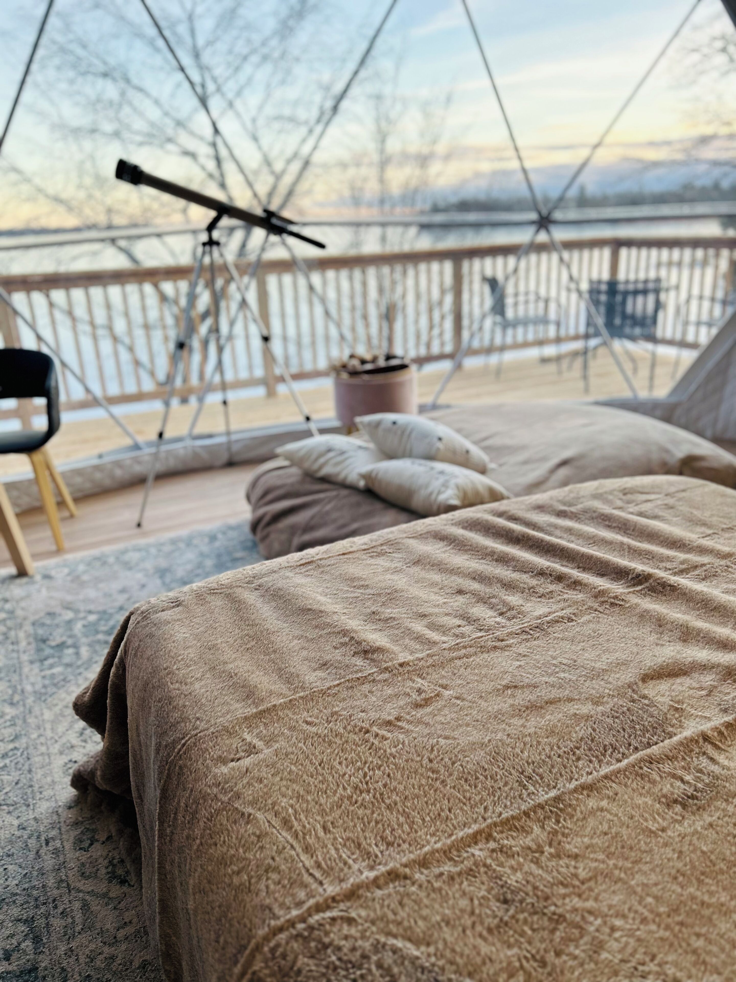 Una habitación acogedora con una cama, una silla y un telescopio en un balcón.