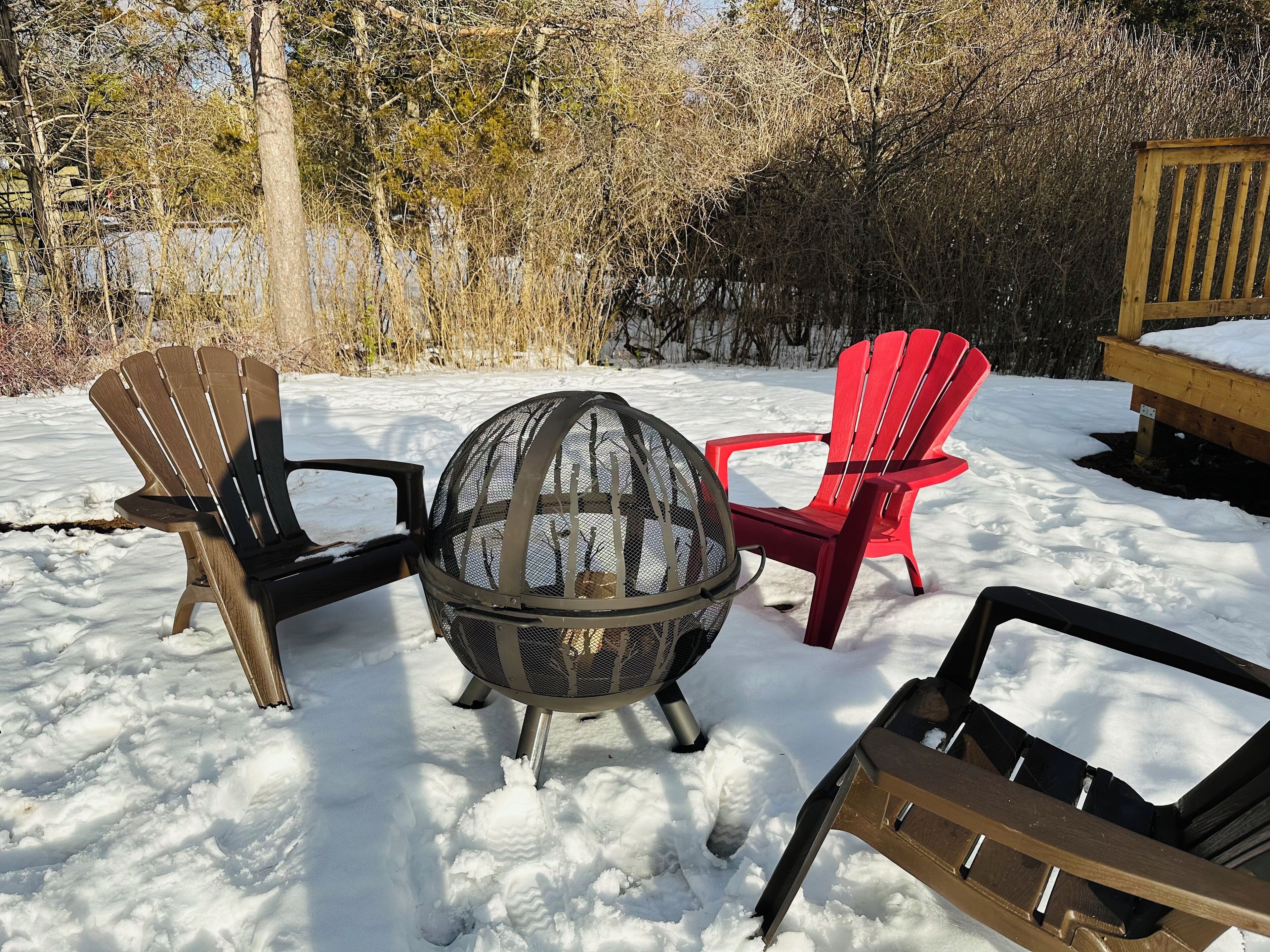 Un espace extérieur aménagé avec des sièges, recouvert de neige, comprenant des fauteuils Adirondack et un foyer.