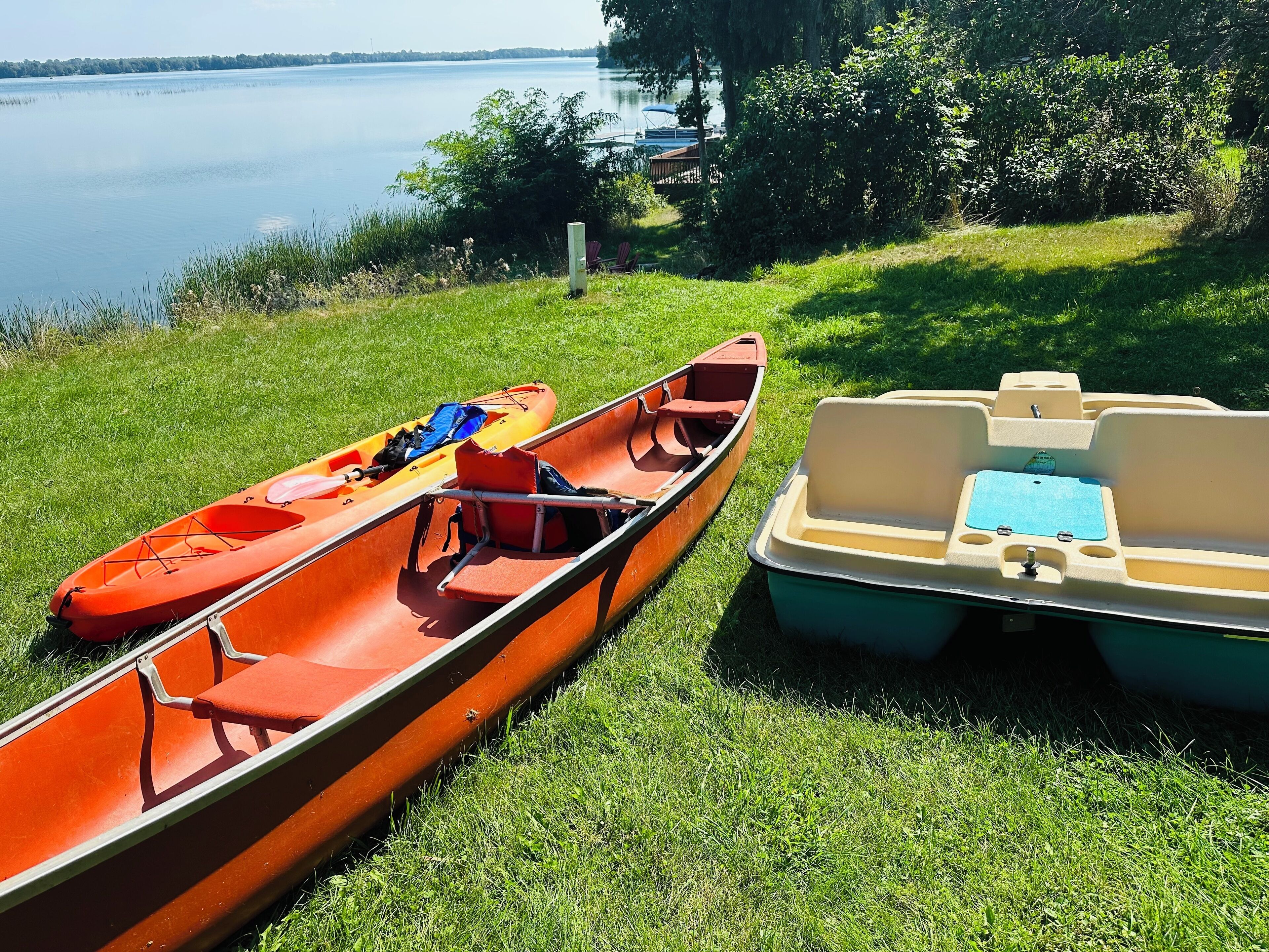 Due kayak e una piccola imbarcazione ormeggiati in un’area erbosa vicino a un lago.