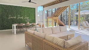 Un espacio exterior moderno con pared verde, mobiliario de mimbre y una escalera que conduce a un nivel superior.