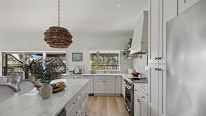 Una cocina moderna con armarios blancos, encimera de mármol y una lámpara de mimbre colgante.