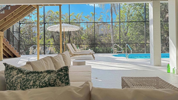 Un área de piscina interior moderna con un ventanal grande, techo de madera y un sofá con cojines estampados.