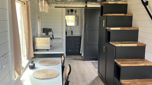 Una cocina moderna con una isla central, muebles oscuros y una escalera de madera.