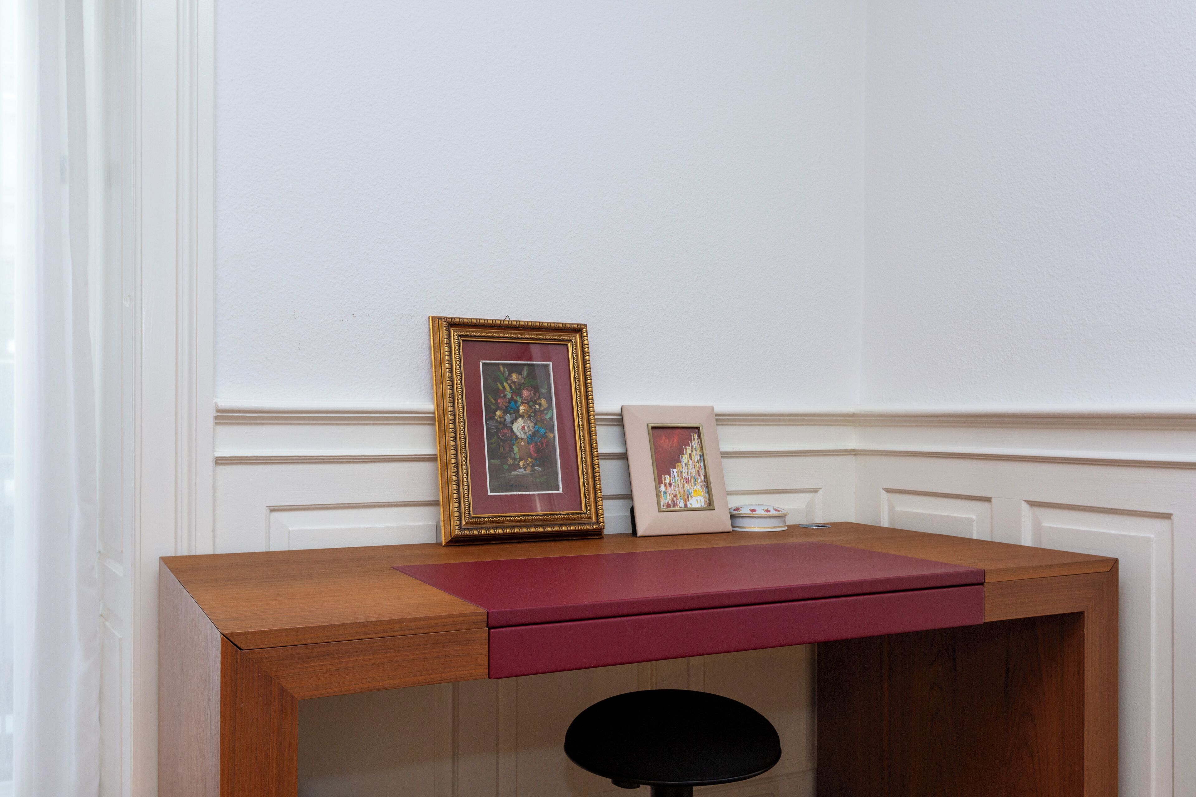 Een houten bureau met een rode lade, twee lijstjes met foto's en een kaars aan de rechterkant.