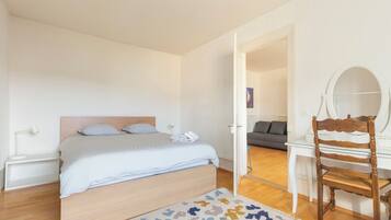 Un dormitorio con una cama, una mesita de noche, una silla, un espejo y una puerta que da a otra habitación.