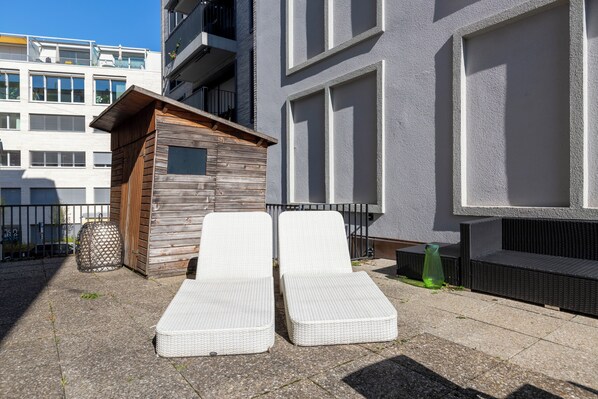 Une petite structure en bois avec deux fauteuils blancs à l’extérieur d’un bâtiment moderne.