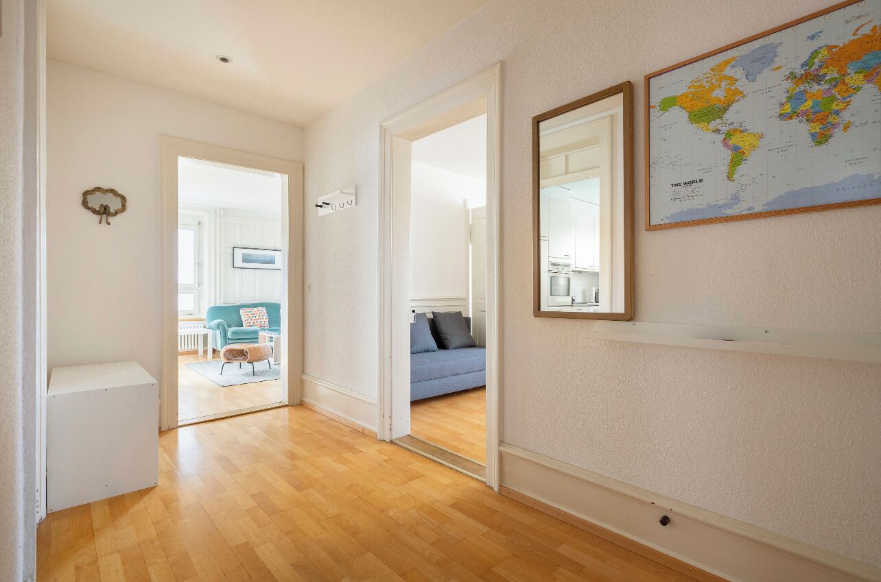 A hallway with wooden flooring leading to a living area with a blue sofa and a world map on the wall.