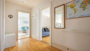 A hallway with wooden flooring leading to a living area with a blue sofa and a world map on the wall.
