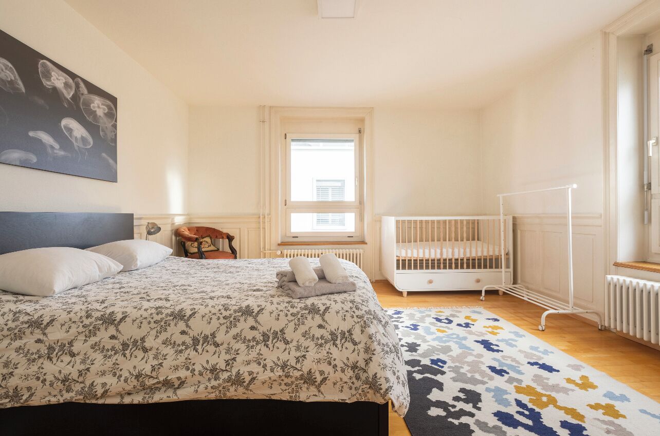 Un dormitorio con una cama, una cuna, una ventana y un radiador.