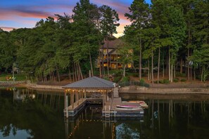 A lakeside property with a dock, a covered seating area, and a house surrounded by tall trees. - Livin' Large Lake Norman Estate w/ Pool, Dock, Game Room & Scenic Views (Mooresville)