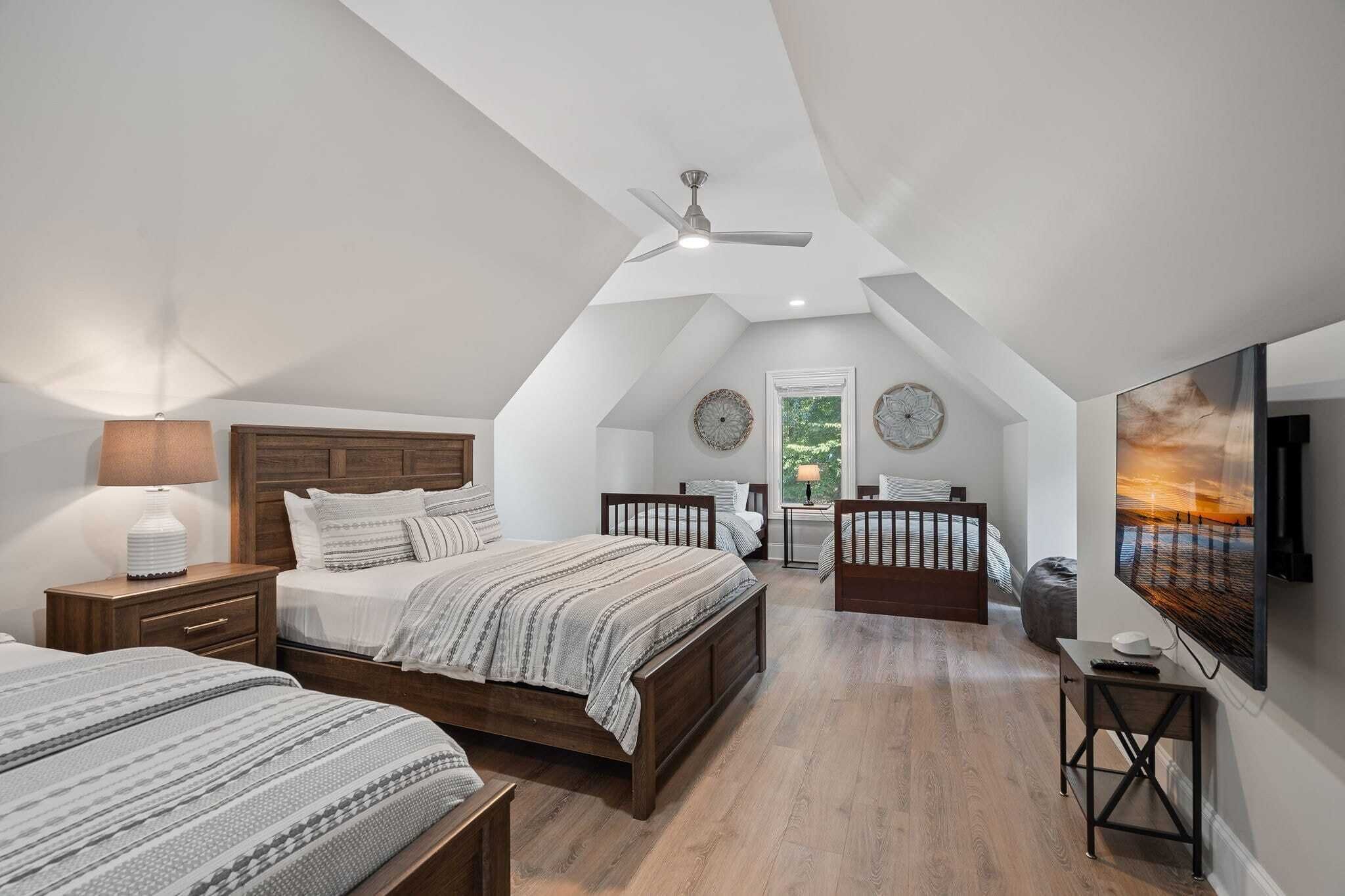 Une chambre avec un plafond en pente, une tête de lit en bois, deux lits, une table de chevet, une lampe, un téléviseur et un tableau.