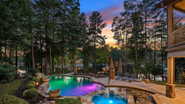 Piscina con hidromasaje, rodeada por una terraza de piedra y sillones de descanso, con árboles altos y un atardecer de fondo.