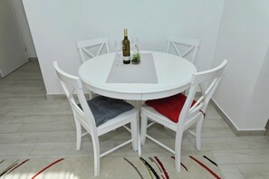A round white table with four chairs, a bottle of wine, and two glasses on a white placemat. - Apartment Donat  (Zadar)