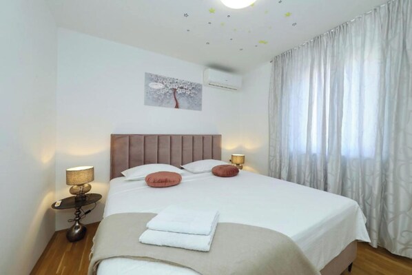 A neatly made bed with pillows, a bedside lamp, and a wall-mounted air conditioner. - Apartment Donat  (Zadar)