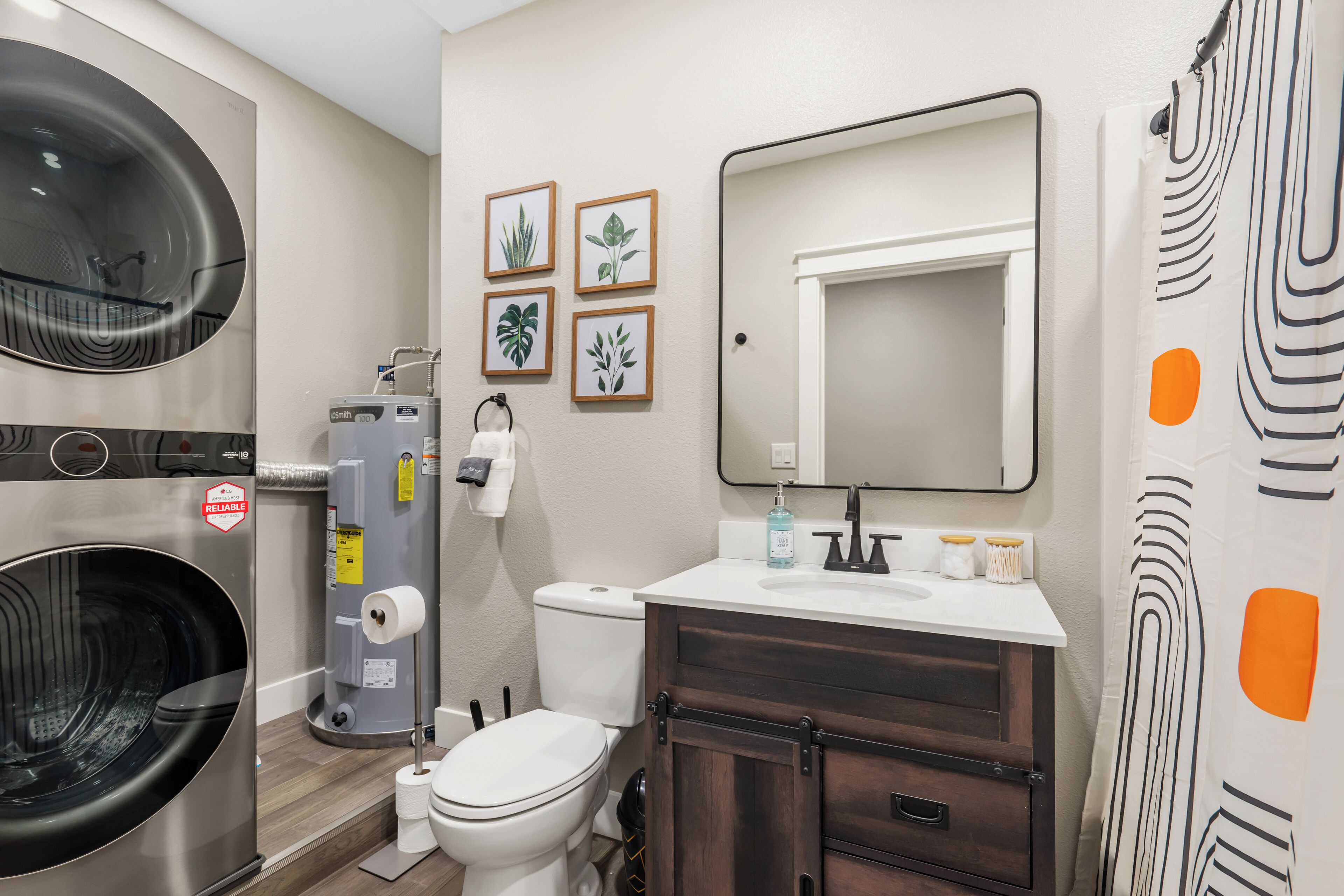 A bathroom with a washing machine, a toilet, a sink with a mirror, and framed plant pictures on the wall.