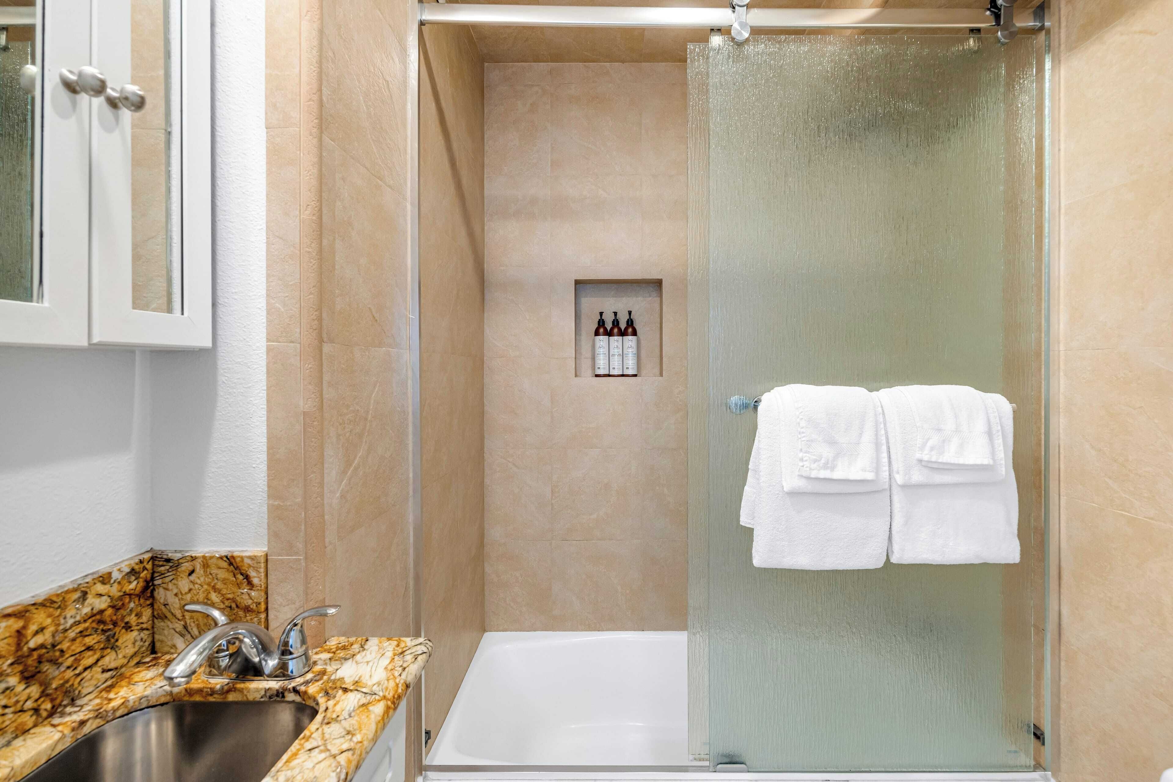 A modern bathroom with a glass-enclosed shower, a marble sink, and a small shelf with toiletries.