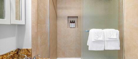 A modern bathroom with a glass-enclosed shower, a marble sink, and a small shelf with toiletries.