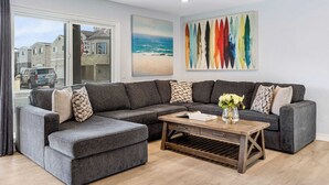 Una sala moderna con un sofá seccional gris, una mesa de centro de madera y un cuadro con temática marina.