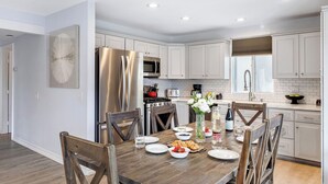 Una cocina moderna con armarios blancos, electrodomésticos de acero inoxidable y una mesa de comedor de madera para cuatro comensales.