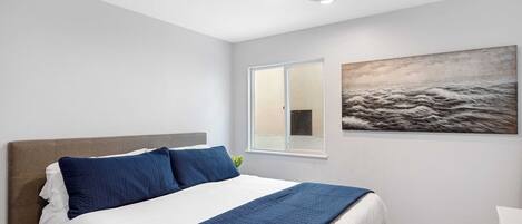A bedroom with a bed, a ceiling fan, a window, and a painting on the wall.