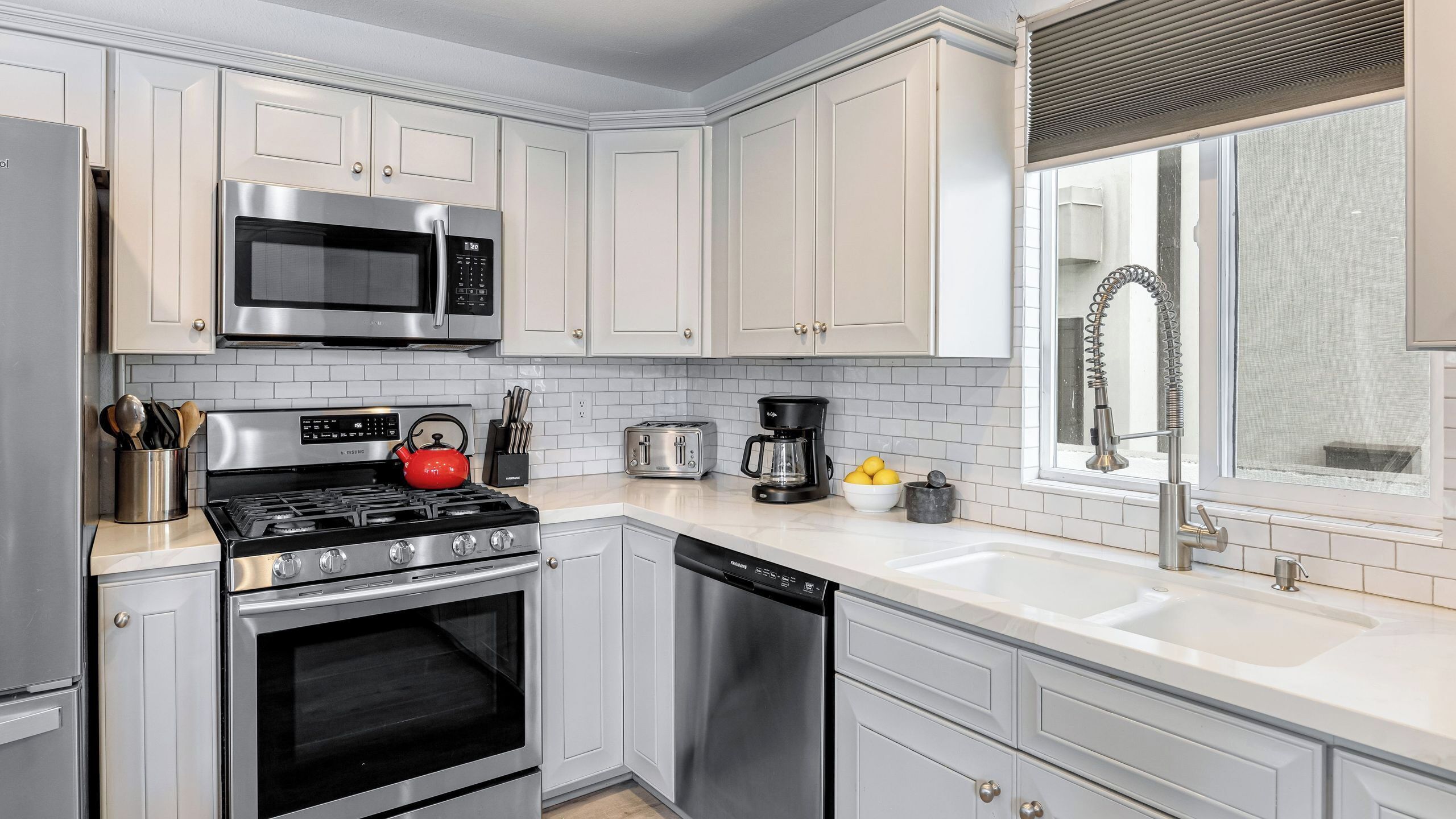 A modern kitchen with stainless steel appliances, white cabinetry, and a large window with a view.
