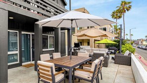 Un patio al aire libre con mesa y sillas de madera, una parrilla y sombrillas.