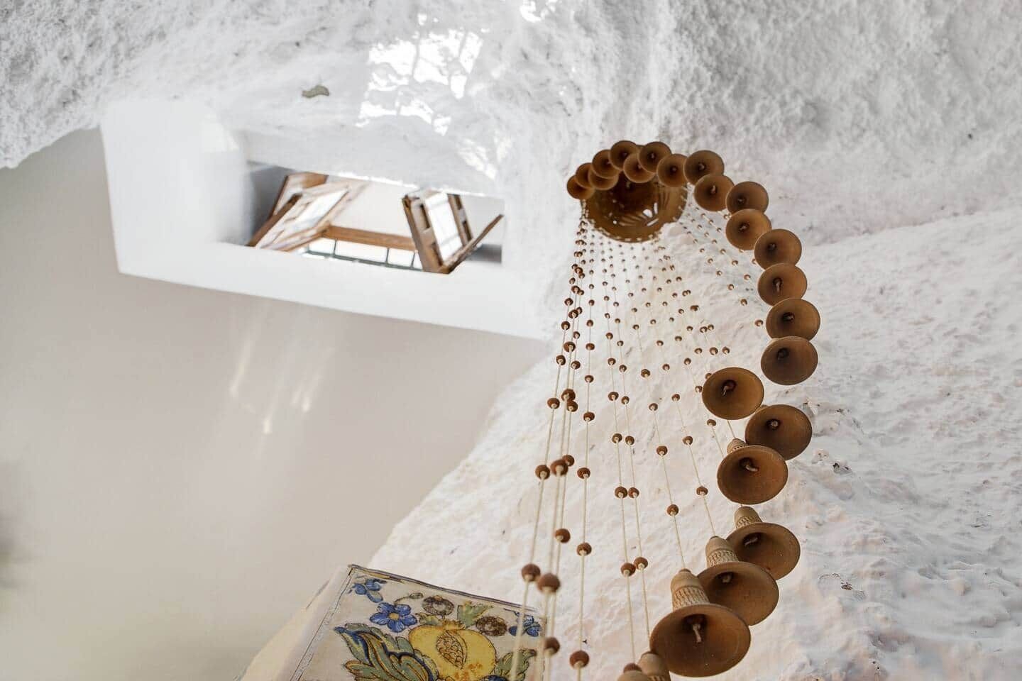 A room with a hanging wooden bell chime, a white wall, and a small shelf with a framed picture.