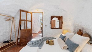 A cozy bedroom with a bed, a wooden door, a small mirror, and a lamp.
