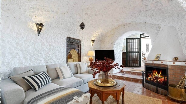 A cozy living room with a white textured wall, a fireplace, a sofa, and a coffee table with a vase.