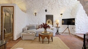 A cozy living room with a white textured wall, a sofa, a coffee table, and a TV on a tripod. - Comeback La Cueva del Gato (granada)