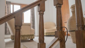A wooden staircase with a handrail, leading to a room with a chair and a large vase.