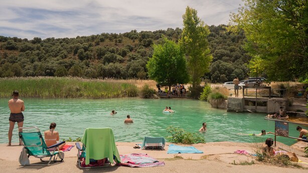 A natural pool surrounded by trees and a hill. People are swimming and relaxing in the water.