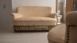 A beige sofa with a fringed throw in a room with light-colored flooring and a wooden door in the background.