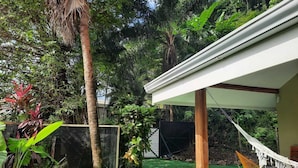 A covered outdoor area with a hammock, a hammock chair, and a small table. - Casa Mor - Surfhouse 2 min to the beach (Cóbano)