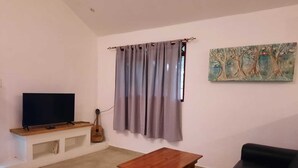 A living room with a flat-screen TV, a wooden coffee table, a black sofa, a guitar, and a window with grey curtains. - Casa Mor - Surfhouse 2 min to the beach (Cóbano)