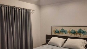 A neatly made bed with a light-colored bedspread and two pillows, a wooden headboard, and a wall with a leaf-patterned artwork. - Casa Mor - Surfhouse 2 min to the beach (Cóbano)