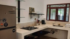 A compact kitchen with a refrigerator, stove, sink, and a window with a view. - Casa Mor - Surfhouse 2 min to the beach (Cóbano)
