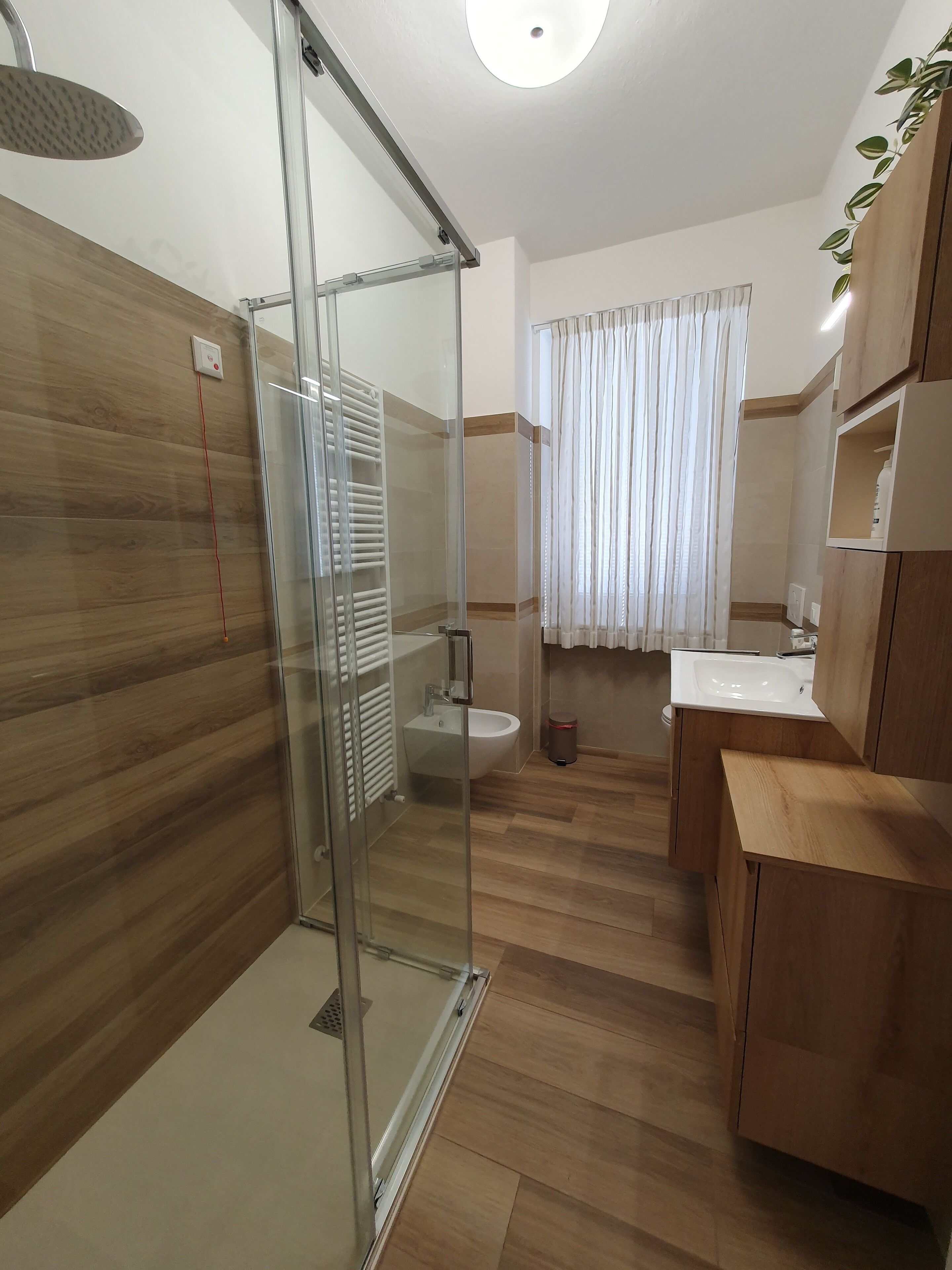 Un baño moderno con cabina de ducha de vidrio, un bidé, un lavamanos y armarios de madera.