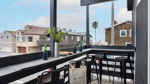 Un balcon donnant sur des immeubles d’habitation, une plante en pot et une table avec des chaises et des bouteilles.