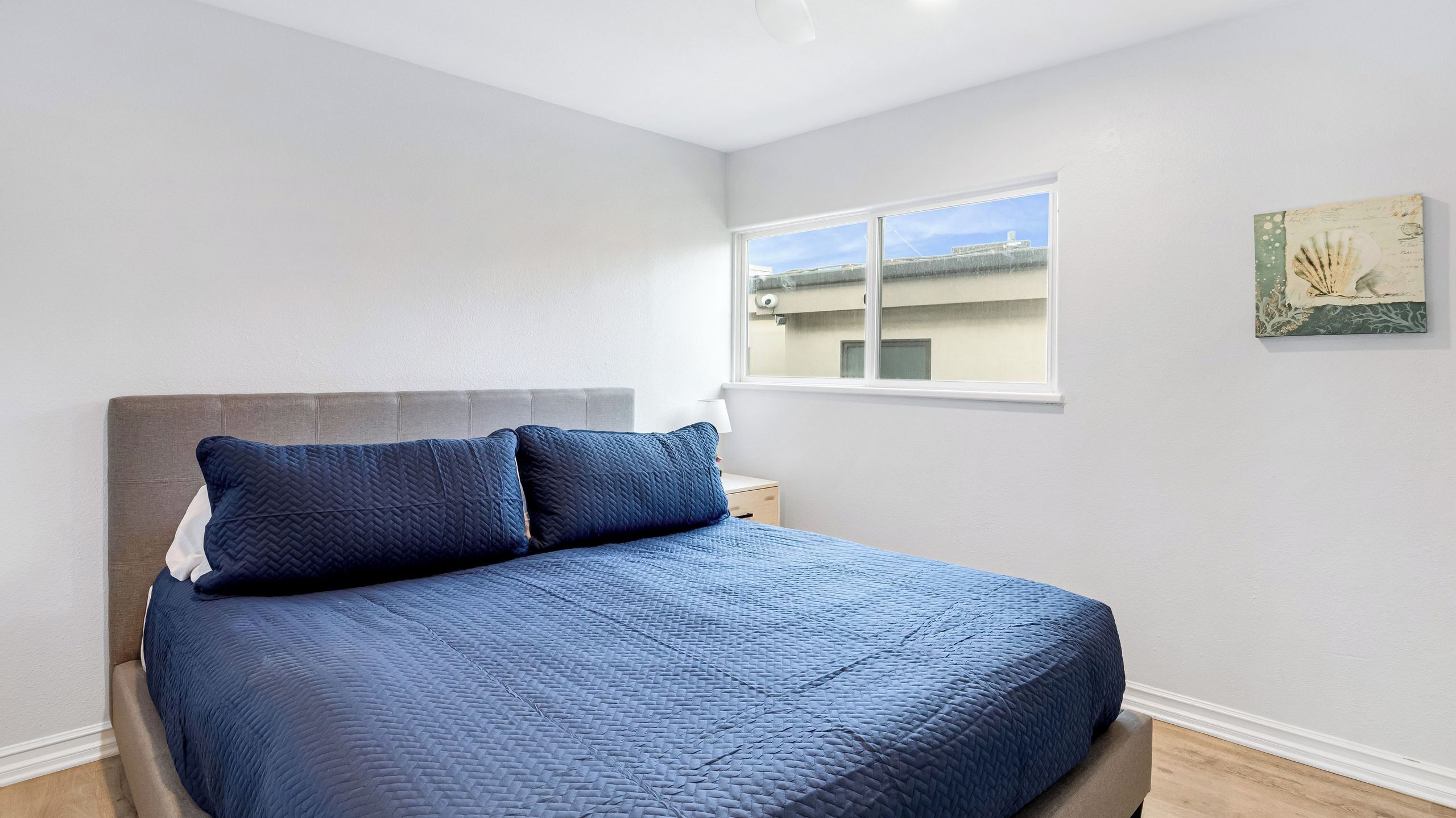 A bedroom with a bed, a nightstand, a window, and a wall art piece.