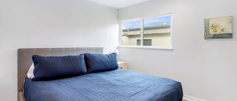A bedroom with a bed, a nightstand, a window, and a wall art piece.