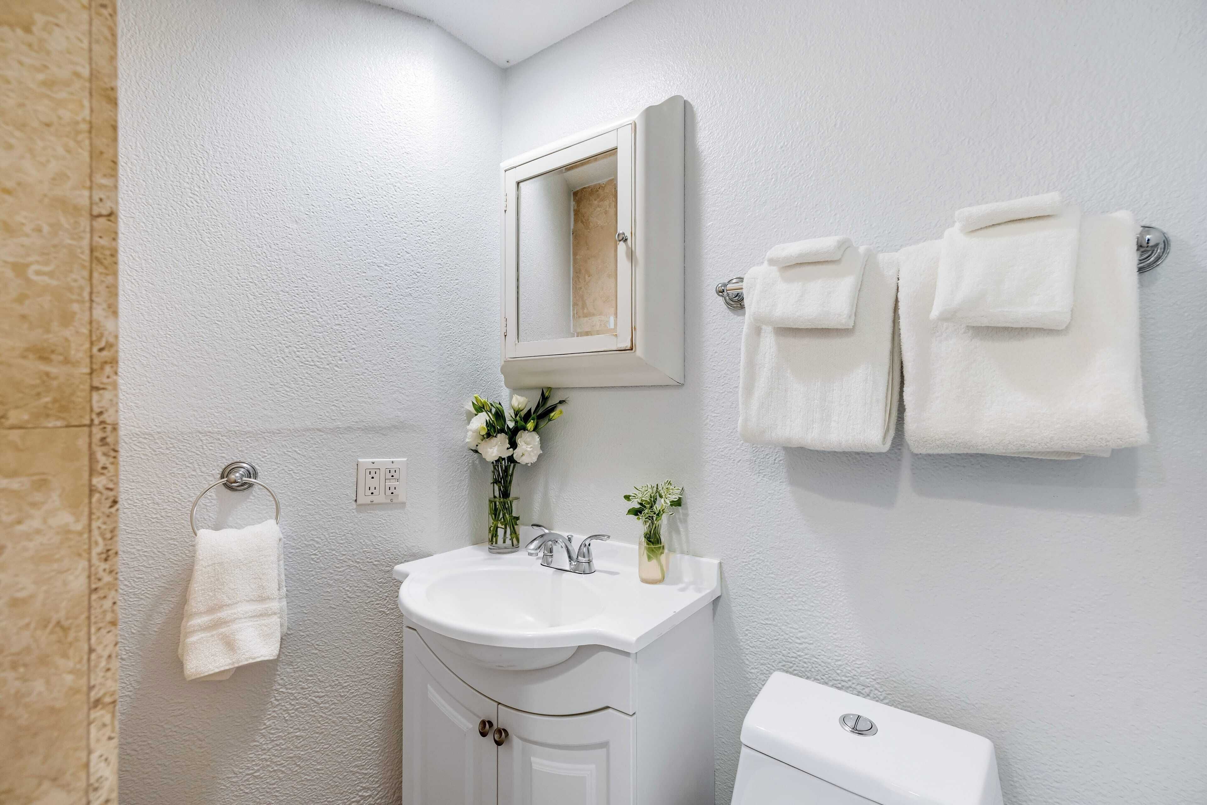 Un baño con un lavamanos blanco, un espejo y dos toallas colgadas en la pared.