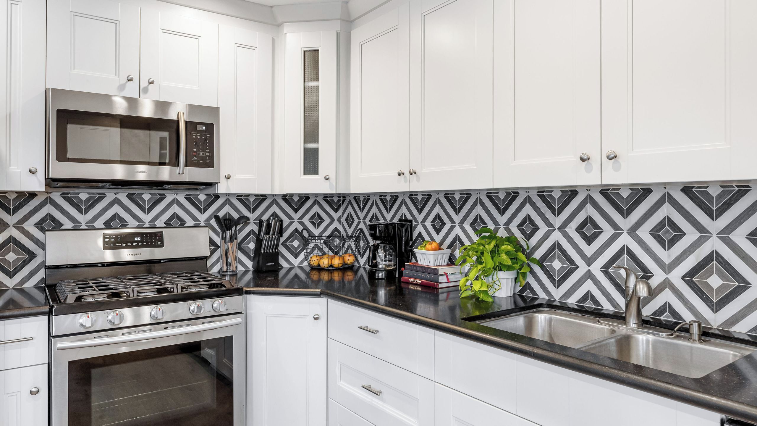 A modern kitchen with white cabinets, stainless steel appliances, a patterned backsplash, and a black countertop.