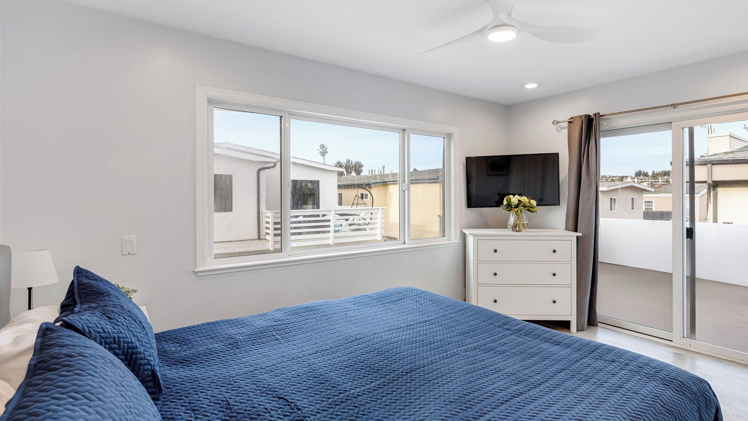 Quarto com cama, cômoda, televisão e varanda.