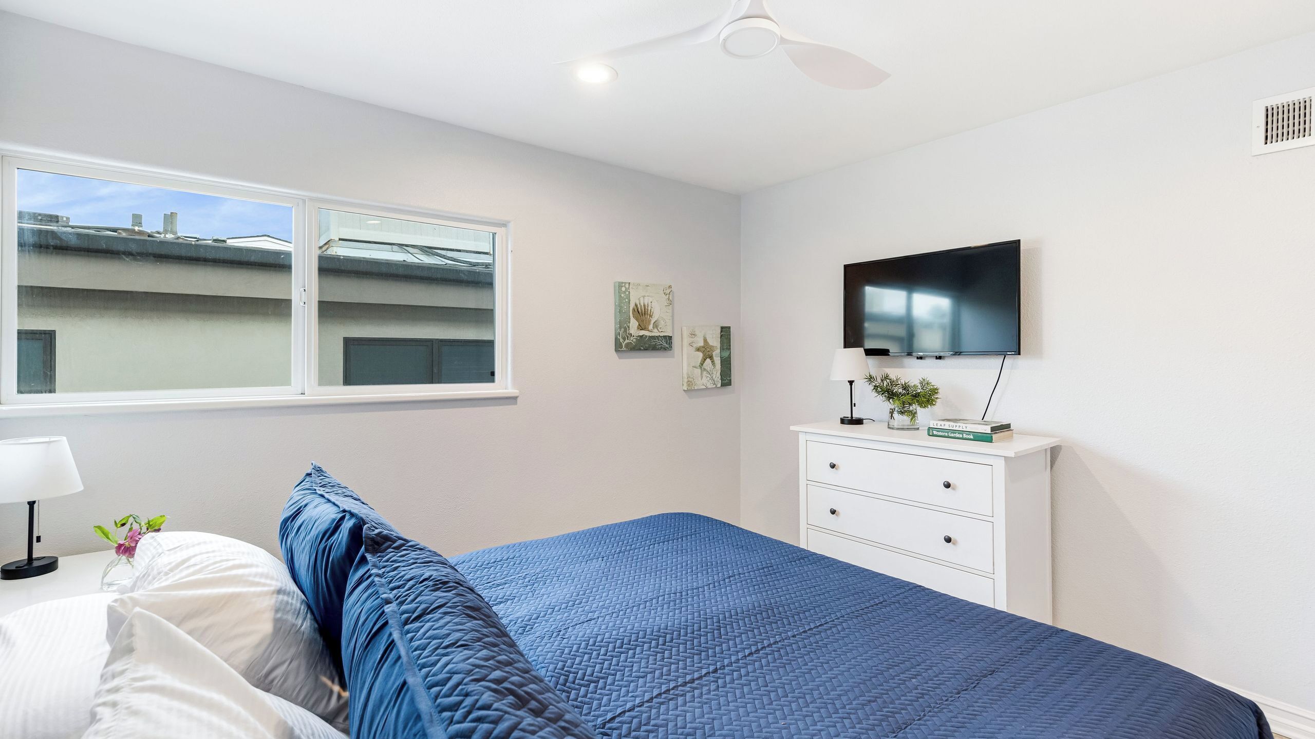 A bedroom with a bed, a dresser, a television, and a window with a view of buildings.