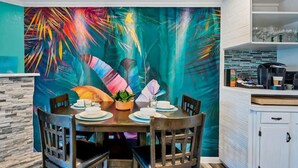 A dining area with a table set for four, a fireplace, and a colorful abstract mural on the wall. - River Front Condo: Close to Downtown and Gruene! (New Braunfels)